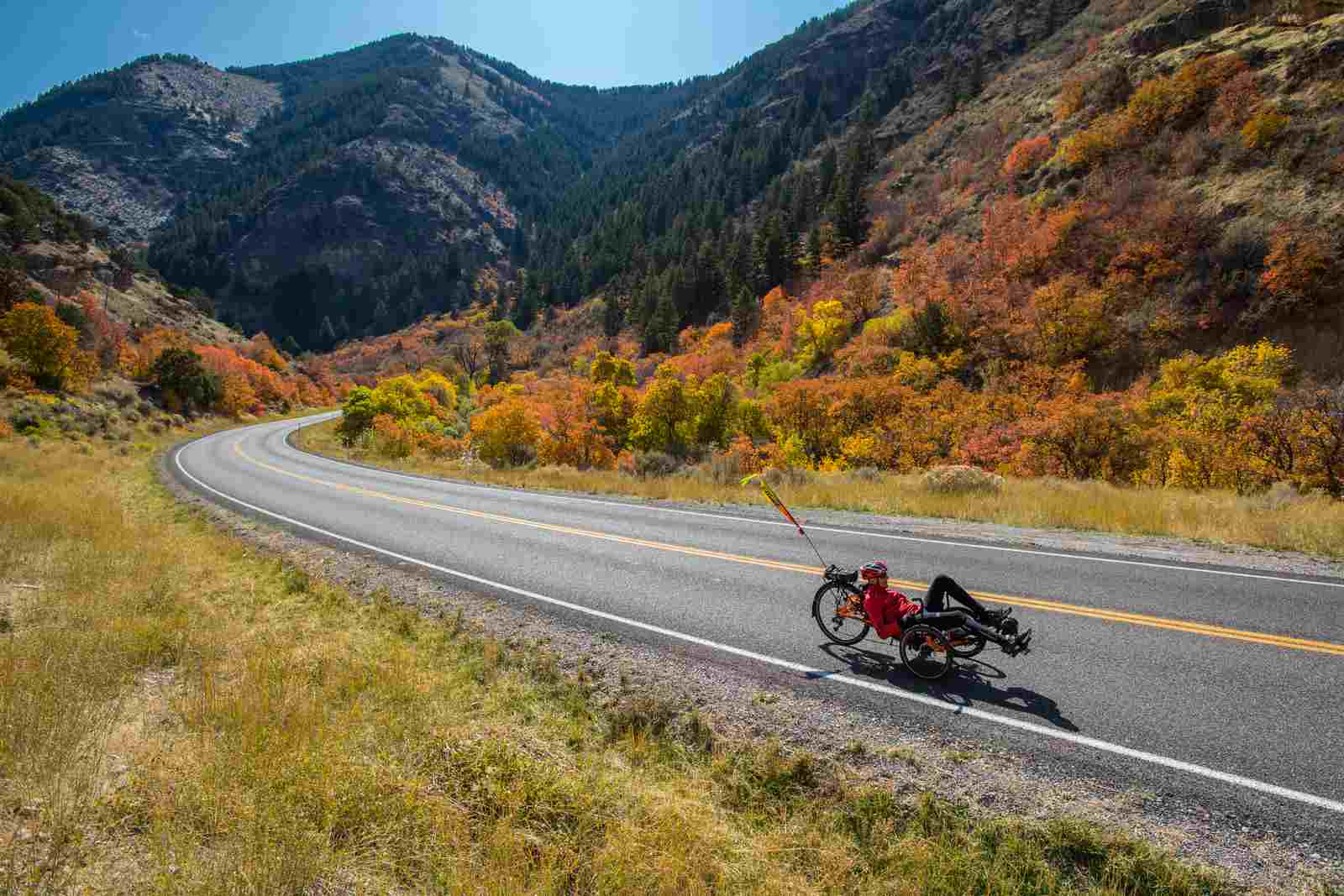 Bicyclist on road through mountains with autumn leaves