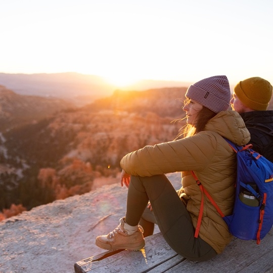 Two people sitting on overlook of red rock canyon at sunrise