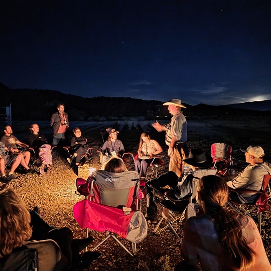 Man talking to a group of people around a campfire at night