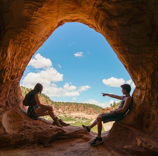 Man and woman sitting in red rock cave looking outward
