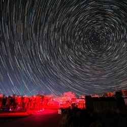 Night sky with stars in rotation above lit up red rock hoodoos